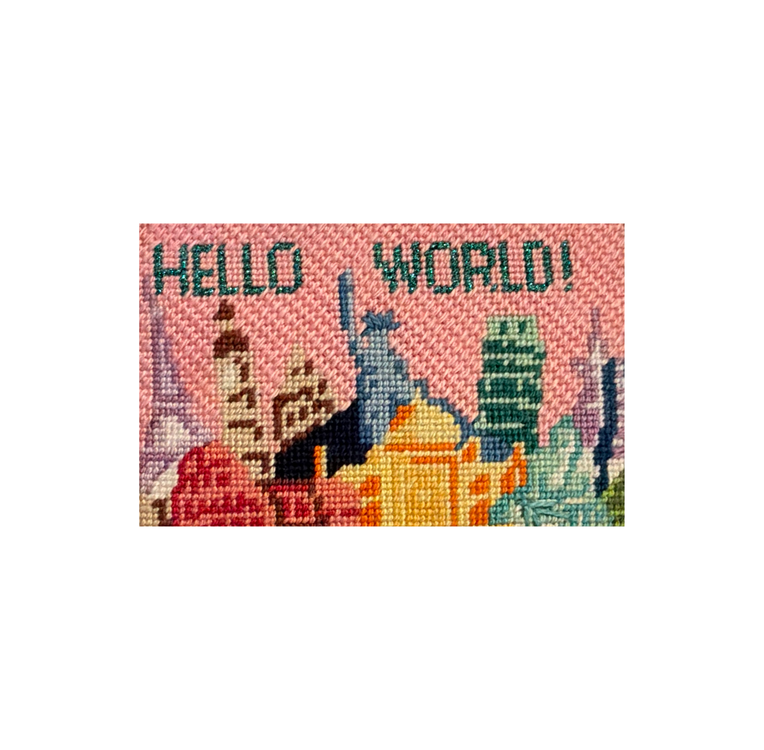 Needlepoint canvas stitched with a pink city skyline reading HELLO WORLD, ready to be finished into FFF leather goods.