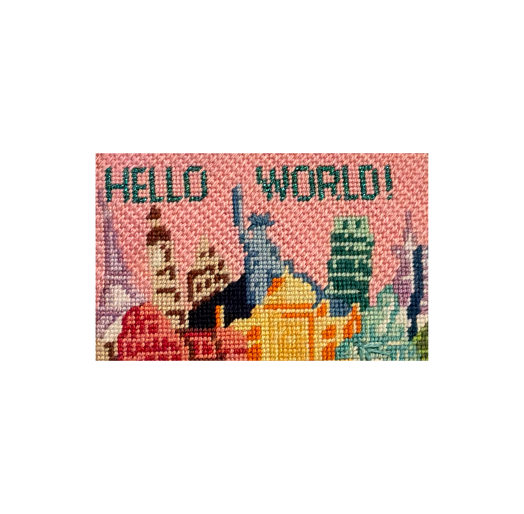 Needlepoint canvas stitched with a pink city skyline reading HELLO WORLD, ready to be finished into FFF leather goods.